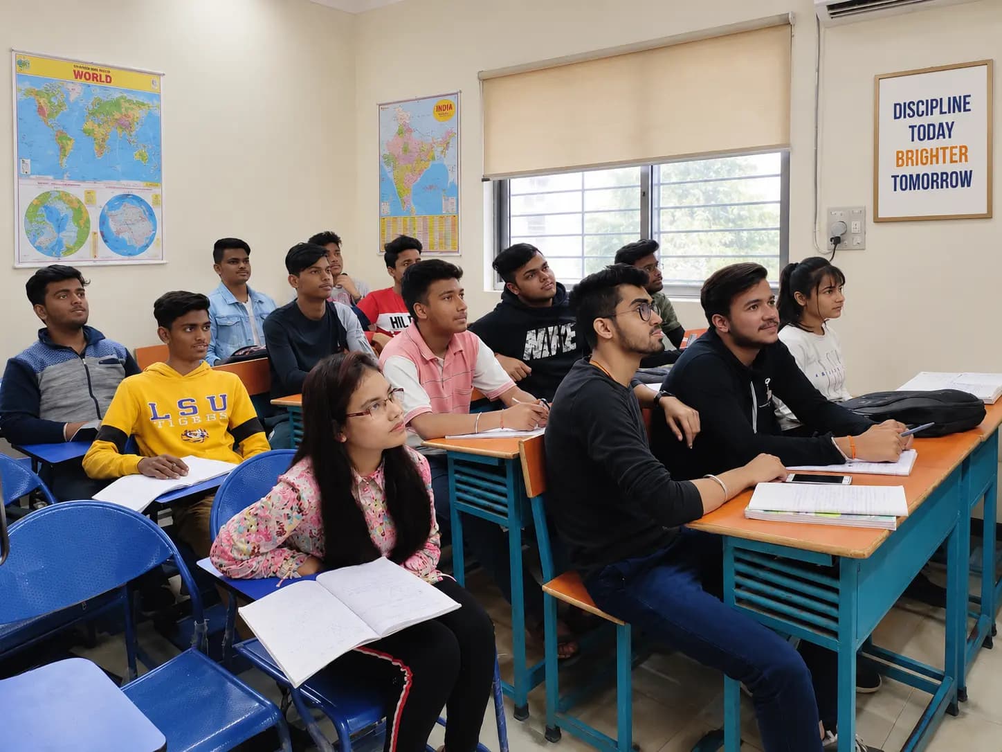 Students seated at classroom desks with notebooks, listening attentively